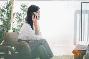 un alegre mujer Comparte un risa en el teléfono, su deleite evidente en su expresión, como ella disfruta un calentar bebida por un iluminado por el sol ventana, creando un escena de comodidad y genuino conexión. foto