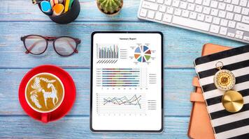 Wooden desk workplace with business chart on screen tablet display, keyboard, notebook, eyeglass and cup of coffee, Top view flat lay. photo