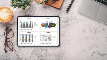 oficina escritorio lugar de trabajo con negocio gráfico en tableta mostrar, computadora portátil, lente, computadora portátil, bolígrafo y taza de café, parte superior ver plano laico con Copiar espacio. foto