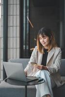 A professional woman takes a short break for some online shopping, focused on her laptop while holding a credit card, combining work with personal time in a modern office setting. photo