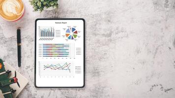 Office desk workplace with business chart on screen tablet display, notebook, pen and cup of coffee, Top view flat lay with copy space. photo