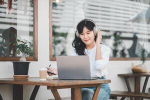 A content remote worker enjoys a peaceful outdoor work session, wearing headphones and engaging with a laptop, complemented by a warm beverage and natural surroundings. photo