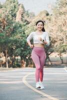 A joyful runner wearing pink leggings and white sneakers exudes happiness and health while jogging on a park path, surrounded by greenery. photo