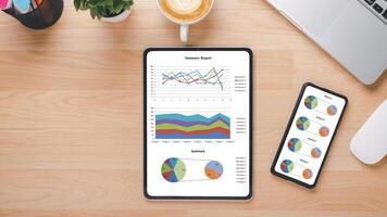 An overhead shot of a workspace showcasing an efficient analysis setup, with a tablet displaying colorful charts and a smartphone with pie charts, paired with a laptop and a cup of coffee. photo