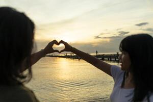 dos asiático adolescente mano haciendo un corazón forma dedo en contra hermosa ligero de puesta de sol cielo foto