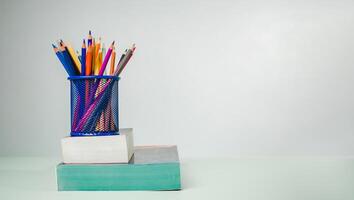 Stack of colorful textbooks and a glass of bright pencils on a white background, Concept of education, training, School tools, workspace, copy space, Banner design education concept background. photo