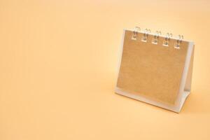 Blank calendar with brown paper isolated on orange background. Blank paper desk spiral calendar. close up of a blank recycle paper template. photo