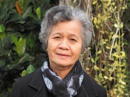 Senior Asian woman with short white hair smiling and looking at the camera while standing in a garden. Space for text. Concept of aged people and healthcare photo