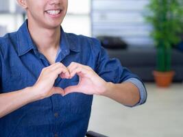 Close-up of a young man making a heart shape with fingers. Concept of couple and love. Valentine's day. Space for text photo