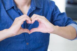 Close-up of a young man making a heart shape with fingers. Space for text. Concept of celebrating Valentine's Day photo