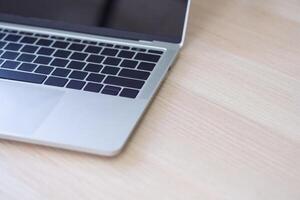 A close-up of the side view of the laptop is placed on the wooden table in the office. Space for text photo