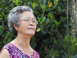 Senior Asian woman with short white hair smiling and looking away while standing in a garden. Space for text. Concept of aged people and healthcare photo