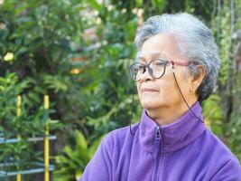 Senior Asian woman with short white hair smiling and looking away while standing in a garden. Space for text. Concept of aged people and healthcare photo