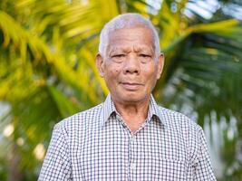 Portrait of an elderly Asian man smiling and looking at the camera while standing in a garden. Space for text. Concept of aged people and healthcare photo