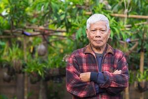 Portrait of elderly Asian man arms crossed and looking at the camera while standing in a garden. Space for text. Concept of aged people and healthcare photo