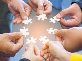 Top view of many people hands holding a jigsaw puzzle piece in a circle together with sunlight effect. Concept of teamwork and unity photo