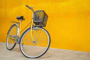 Yellow retro bicycle against a yellow wall. Vintage woman bike with a basket in front. Space for text photo