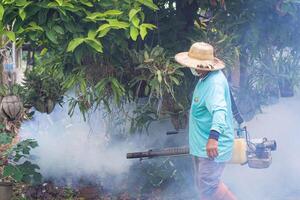 un hombre es trabajando empañamiento a eliminar mosquitos en el lluvia, temporada ser Cuidado de mosquitos y proteger en contra dengue fiebre desparramar. concepto de cuidado de la salud foto