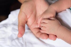 Hands of newborn baby in the hand of mother on white cloth. Close-up of baby hands. Space for text. Family concept photo