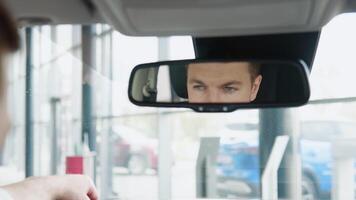 Elegant man looks at the car mirror of his new car in a car dealership video