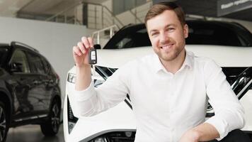 A man with keys rejoices in buying a new electric car in a car dealership video