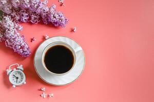 Alarm clock, lilac flowers and cup of coffee on light background. photo