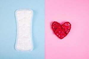 Sanitary pad and red heart on colored background. Menstruation and womens health. photo