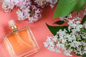 Perfume bottle and lilac flowers on pink background. photo