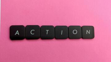 The word Action spelled out in black plastic buttons on a pink background photo