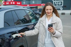 Young business woman refueling her electric car at a EV charging station. Concept of environmentally friendly vehicle. Electric car concept. Green travelling. photo