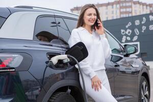 joven mujer utilizando un teléfono inteligente a pagar para eléctrico coche a el cargando estación. recarga batería desde cargando estación. foto