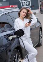 Young woman charging her electric car at a charging station in the city. Eco fuel concept. The concept of environmentally friendly transport. Recharging battery from charging station. photo