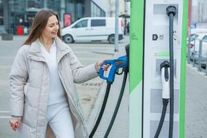 Young business woman refueling her electric car at a EV charging station. Concept of environmentally friendly vehicle. Electric car concept. Green travelling. photo