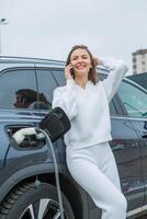 joven negocio mujer repostaje su eléctrico coche a un ev cargando estación. concepto de ambientalmente simpático vehículo. eléctrico coche concepto. verde de viaje. foto