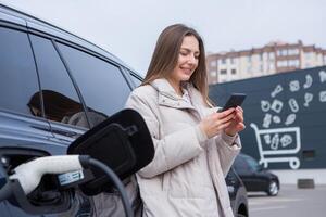 joven hermosa mujer de viaje por eléctrico coche teniendo detener a cargando estación. eléctrico coche concepto. verde de viaje. foto