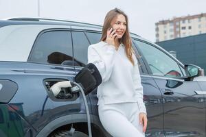 Young business woman refueling her electric car at a EV charging station. Concept of environmentally friendly vehicle. Electric car concept. Green travelling. photo