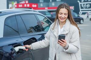 Young business woman refueling her electric car at a EV charging station. Concept of environmentally friendly vehicle. Electric car concept. Green travelling. photo