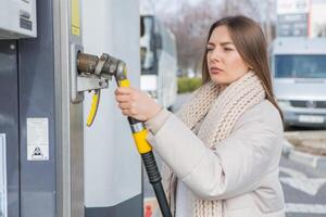 joven mujer participación un combustible boquilla en su mano mientras repostaje coche a gas estación. un detener para repostaje a el gas estación. alimentando el coche con gas. foto