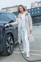 Young business woman refueling her electric car at a EV charging station. Concept of environmentally friendly vehicle. Electric car concept. Green travelling. photo