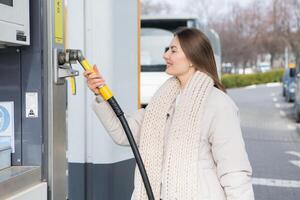 joven mujer participación un combustible boquilla en su mano mientras repostaje coche a gas estación. un detener para repostaje a el gas estación. alimentando el coche con gas. foto