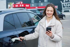 Young business woman refueling her electric car at a EV charging station. Concept of environmentally friendly vehicle. Electric car concept. Green travelling. photo