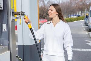 joven mujer participación un combustible boquilla en su mano mientras repostaje coche a gas estación. un detener para repostaje a el gas estación. alimentando el coche con gas. foto