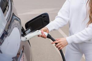 Young woman charging her electric car at a charging station in the city. Eco fuel concept. The concept of environmentally friendly transport. Recharging battery from charging station. photo