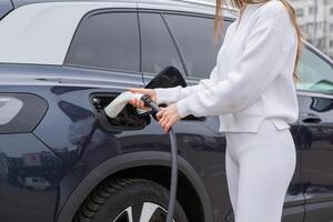 Young woman charging her electric car at a charging station in the city. Eco fuel concept. The concept of environmentally friendly transport. Recharging battery from charging station. photo