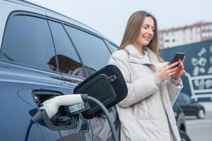 Young business woman refueling her electric car at a EV charging station. Concept of environmentally friendly vehicle. Electric car concept. Green travelling. photo