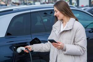 Young woman charging her electric car at a charging station in the city. Eco fuel concept. The concept of environmentally friendly transport. Recharging battery from charging station. photo