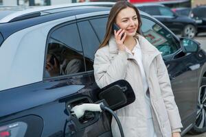 Young business woman refueling her electric car at a EV charging station. Concept of environmentally friendly vehicle. Electric car concept. Green travelling. photo