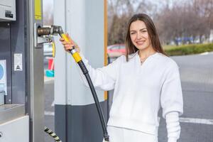 joven mujer participación un combustible boquilla en su mano mientras repostaje coche a gas estación. un detener para repostaje a el gas estación. alimentando el coche con gas. foto