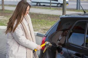 Young woman holding a fuel nozzle in her hand while refueling car at gas station. A stop for refueling at the gas station. Fueling the car with gas. photo