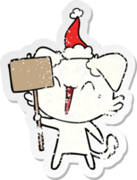 happy little hand drawn distressed sticker cartoon of a dog holding sign wearing santa hat png